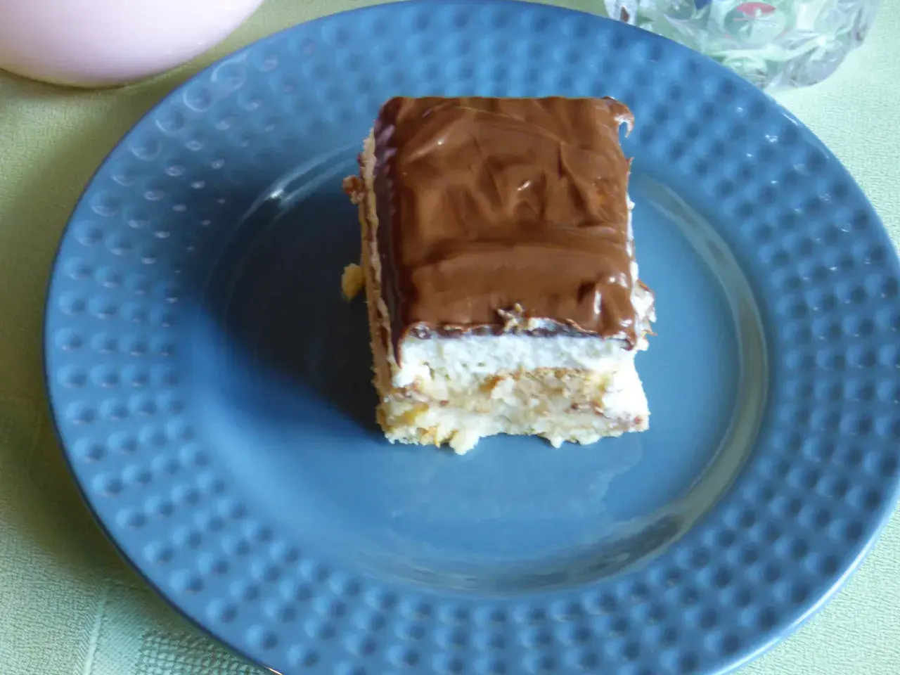 Pyszne ciasto Kinder Bueno z mascarpone, polane czekoladą, na niebieskim talerzu.