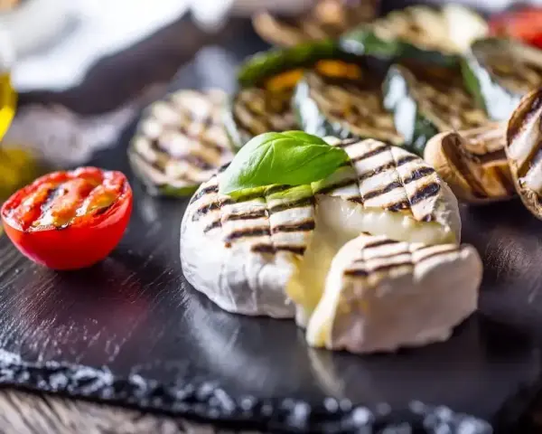 Pyszny camembert z grilla, z rumianymi paskami, podany z grillowanymi warzywami i pomidorkiem.