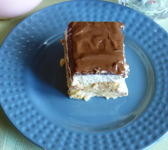 Pyszne ciasto Kinder Bueno z mascarpone, polane czekoladą, na niebieskim talerzu.